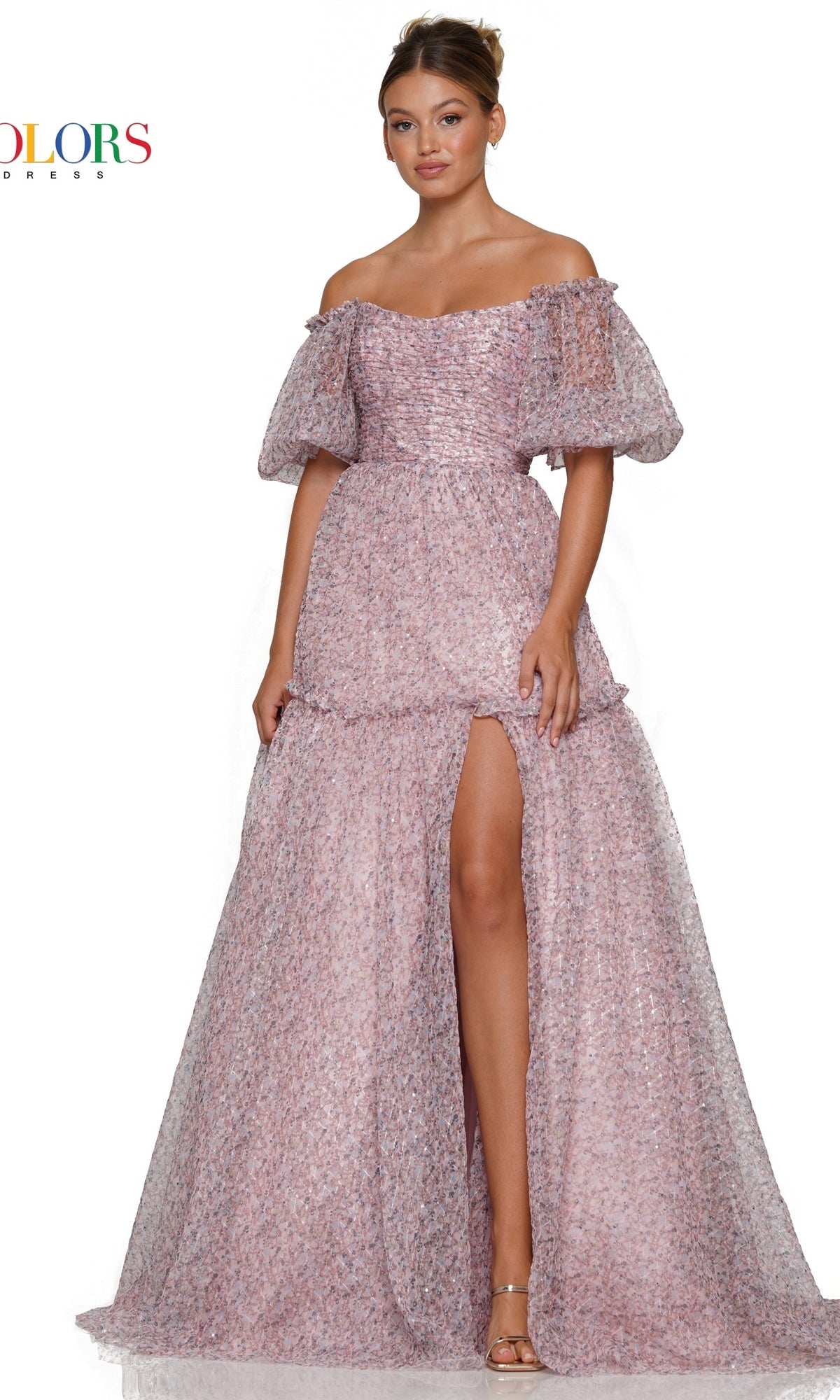 A woman stands against a white background wearing the Colors Dress Long A-Line Prom Dress 3190 with puff sleeves and a high slit. The textured pink off-the-shoulder gown offers an elegant, feminine silhouette perfect for prom night.